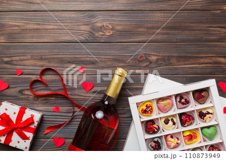 Bottle of red wine on colored background for Valentine Day with gift and chocolate. Heart shaped with gift box of chocolates top view with copy space 110873949