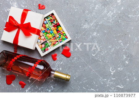Bottle of red wine on colored background for Valentine Day with gift and chocolate. Heart shaped with gift box of chocolates top view with copy space 110873977