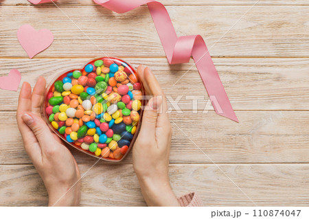 Female hands with delicious candies in box on color background 110874047