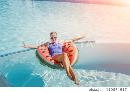 Happy woman in a swimsuit and sunglasses floating on an inflatable ring in the form of a watermelon, in the pool during summer holidays and vacations. Summer concept. 110874917