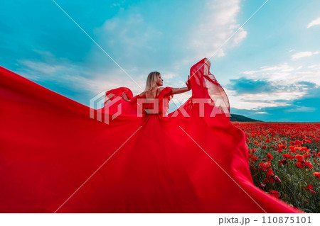 Woman poppy field red dress. Happy woman in a long red dress in a beautiful large poppy field. Blond stands with her back posing on a large field of red poppies Woman poppy field red dress. Happy woman in a long red dress in a beautiful large poppy field. Blond stands with her back posing on a large field of red poppies 110875101