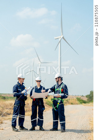 Vertical image of group of professional technician workers stand with discuss the project in the paper plan and stand in front of wind turbine or windmill in area for power plant business. Vertical image of group of professional technician workers stand with discuss the project in the paper plan and stand in front of wind turbine or windmill in area for power plant business. 110875505