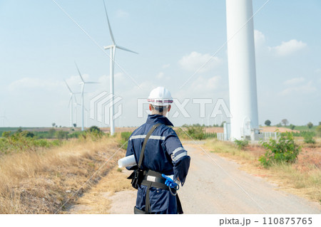 Back of technician worker man stand and look to wind turbine or windmill on the back in area of power plant business. 110875765