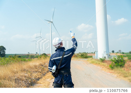 Back of technician worker man stand and point up to the sky and wind turbine or windmill on the back in area of power plant business. 110875766