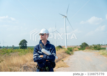 Professional technician worker man stand with arm-crossed and stand with look to his right side in front of wind turbine or windmill in the field and in concept of green energy for good environment. 110875770