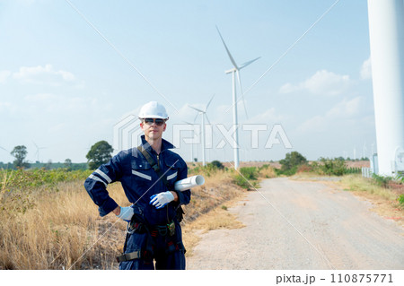 Professional technician worker man stand with hold plan paper and look forward in front of wind turbine or windmill with blue sky in concept of green energy for good environment. Professional technician worker man stand with hold plan paper and look forward in front of wind turbine or windmill with blue sky in concept of green energy for good environment. 110875771