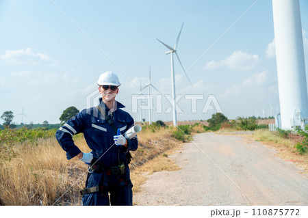 Professional technician worker man with smiling and stand with look at camera in front of wind turbine or windmill with blue sky in concept of green energy for good environment. 110875772