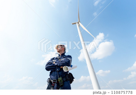 Professional technician worker man stand with arm-crossed and stand in front of wind turbine or windmill with blue sky in concept of green energy for good environment. 110875778