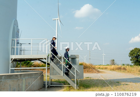 Two of technician workers walk down from stair of base of wind turbine or windmill after finish maintenance work in area of power plant. Two of technician workers walk down from stair of base of wind turbine or windmill after finish maintenance work in area of power plant. 110876219