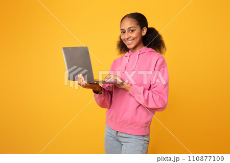 Cheerful black youngster girl with laptop browsing for homework, studio Cheerful black youngster girl with laptop browsing for homework, studio 110877109