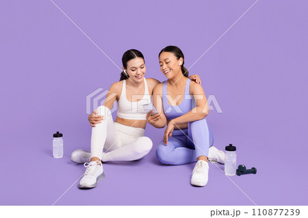 Two diverse women checking a phone during a fitness break, with water bottles Two diverse women checking a phone during a fitness break, with water bottles 110877239