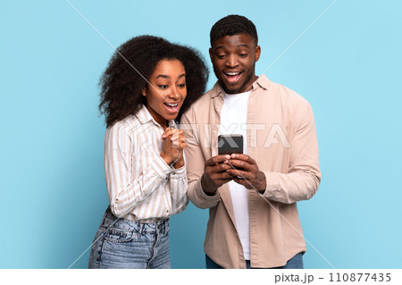 Excited black couple viewing smartphone together on blue background 110877435