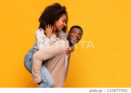 Black man giving piggyback ride to woman on yellow background 110877492