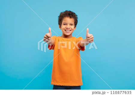 Happy boy giving thumbs up in orange t-shirt, blue background 110877635