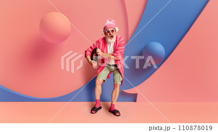 Promotion of active and fun lifestyles of seniors. Lively retirement. Joyful senior man in stylish colorful casual clothes, with headphones dancing 110878019
