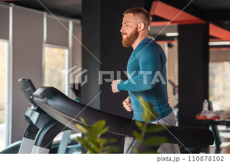 Portrait of a young bearded athletic man training on a treadmill. Copy space. Concept of sport and cardio Portrait of a young bearded athletic man training on a treadmill. Copy space. Concept of sport and cardio 110878102