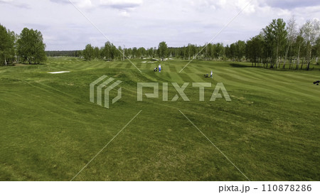 Aerial view Golf course. Golfers walking down the fairway on a course with golf bag and trolley Aerial view Golf course. Golfers walking down the fairway on a course with golf bag and trolley 110878286