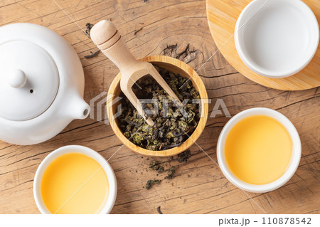 Tea leaves in wood bowl with tea set on wooden table, top view Tea leaves in wood bowl with tea set on wooden table, top view 110878542