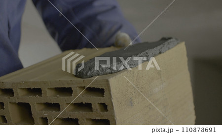 Construction of brick wall. Trowel spreading cement on bricks. Worker spreads cement for bricks 110878691