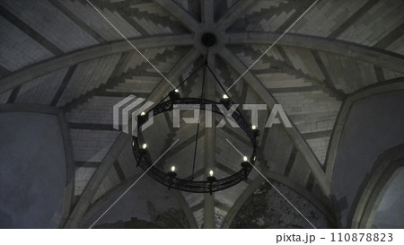 View from the bottom on the old chandelier in the form of a wheel with light bulbs hanging on the ceiling in church or another old building. Action. Beautiful retro style View from the bottom on the old chandelier in the form of a wheel with light bulbs hanging on the ceiling in church or another old building. Action. Beautiful retro style 110878823