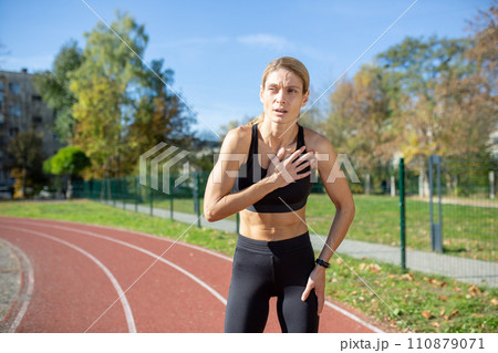 Focused sportswoman taking a break on running track, hands on knees, feeling exhaustion after sprint. Concept of determination and fitness training. 110879071