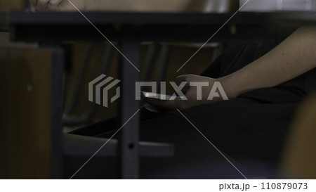 Woman hand using a smart phone under a wooden table. Woman uses the Internet on your phone during the exam 110879073