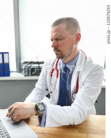 Doctor sits table in office and works with laptop Doctor sits table in office and works with laptop 110879265