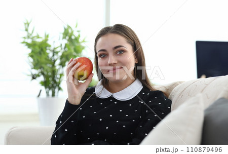 Girl sitting at home couch with apple in her hands Girl sitting at home couch with apple in her hands 110879496
