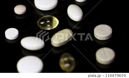 Pills spinning. Pile of several medicines. White tablets with pills on black background. Opened medicine capsule pill 110879659