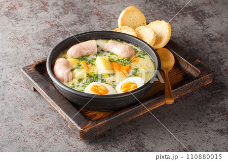 Polish Sour Rye Soup Zurek with white sausage, boiled egg and fresh veggies close-up in a bowl. Horizontal 110880015