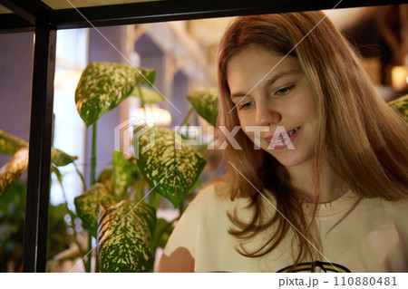 Portrait of cute girl smiling with teeth in dental braces while looking in smartphone against blurred background. Cozy indoor setting. 110880481