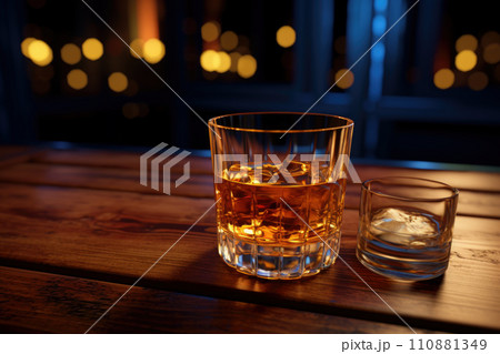 Glass of whiskey with ice cubes served on wooden planks. Vintage countertop with highlight and a glass of hard liquor Glass of whiskey with ice cubes served on wooden planks. Vintage countertop with highlight and a glass of hard liquor 110881349