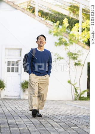 リュックを肩にかけて歩く笑顔の50代の男性　 110883313