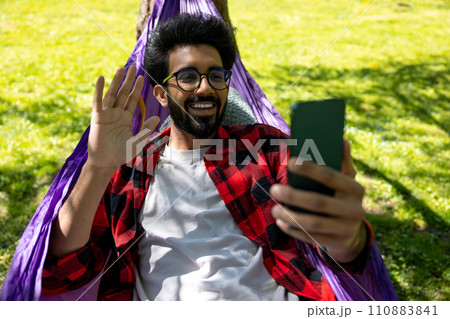 Contented hindu young man talking on the phone and laying in hammock Contented hindu young man talking on the phone and laying in hammock 110883841