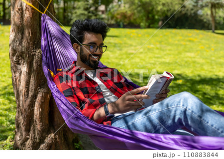 Contented young man in hammock reading a book 110883844