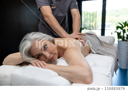 Gray-haired mature woman lying on a couch and having session of back massage 110883879