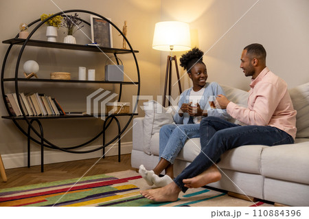 Couple talking drinking tea from glasses sitting on sofa in living room 110884396