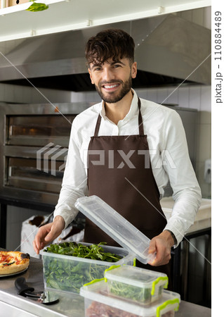Dark-haired bearded young pizzeria worker packing food into containers 110884489