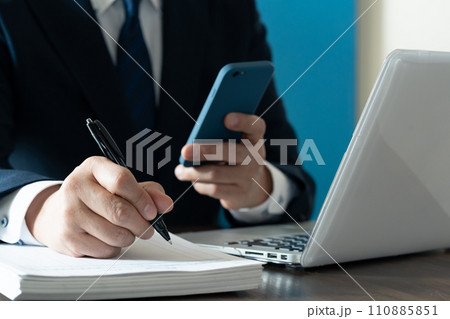 スマホを見てメモを取るビジネスマンの手元 110885851