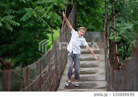A child walks along a suspension bridge over a mountain river. 110886636