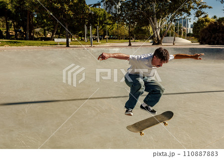 Active young man riding skateboard in skate park on sunny day. Extreme sport concept Active young man riding skateboard in skate park on sunny day. Extreme sport concept 110887883