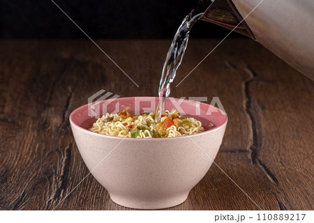 Pouring hot water over dry instant noodles with dry ingredients and spices. 110889217