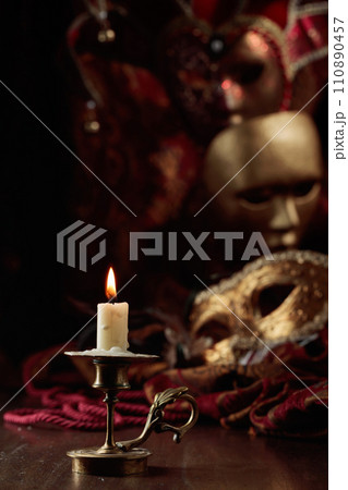 Burning candle in an old brass candlestick and carnival masks. Burning candle in an old brass candlestick and carnival masks. 110890457
