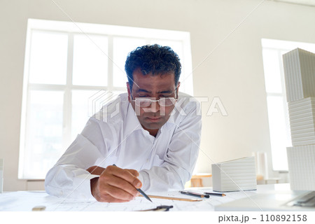 Portrait of male Indian architect drawing sketches at desk in office, copy space 110892158