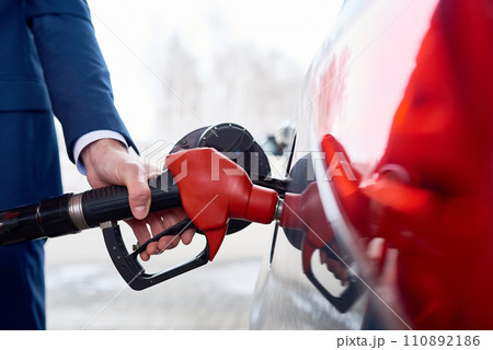 Side view closeup of strong male hand refueling gas tank of luxury car in modern petrol station Side view closeup of strong male hand refueling gas tank of luxury car in modern petrol station 110892186