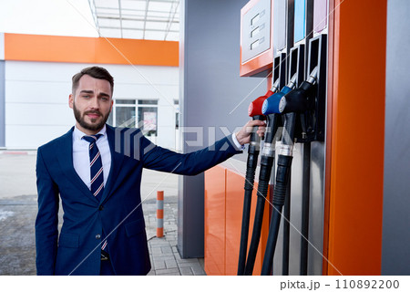 Waist up portrait of young businessman picking up fuel nozzle from pump in modern gas station and looking at camera, copy space Waist up portrait of young businessman picking up fuel nozzle from pump in modern gas station and looking at camera, copy space 110892200