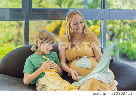 Heartwarming family moment as expectant mom and son joyfully browse through newborn baby's clothes, eagerly anticipating the arrival of a new family member 110892412