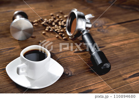 a cup of coffee, coffee beans, a coffee horn and a tamper on a wooden background close-up, selective focus 110894680