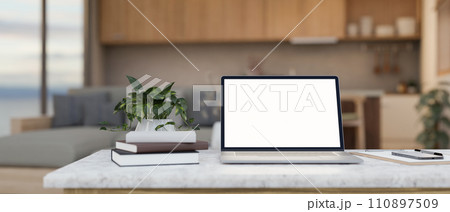 A laptop, books, a potted plant, a phone, and stationery on a table in a modern living room. 110897509