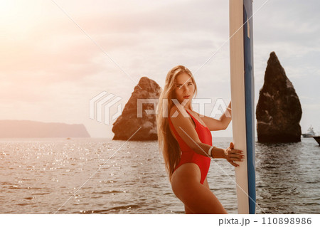 Woman sea sup. Close up portrait of happy young caucasian woman with long hair looking at camera and smiling. Cute woman portrait in bikini posing on sup board in the sea Woman sea sup. Close up portrait of happy young caucasian woman with long hair looking at camera and smiling. Cute woman portrait in bikini posing on sup board in the sea 110898986
